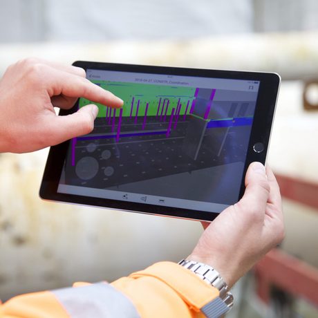 Ein Bauleiter zeigt mit seinem Zeigefinger auf ein iPad auf dem die 3D-Skizze eines Bauwerks abgebildet ist.