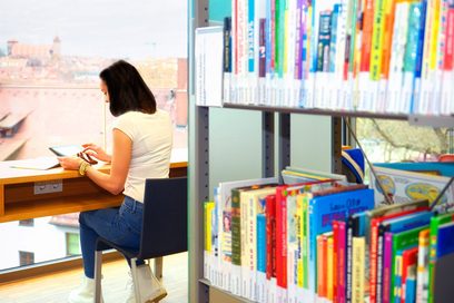 Eine Studentin sitzt in einer Bibliothek und liest.