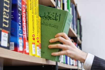 Ein Mann greift nach einem arabischen Sprachbuch in einem Bücherregal.
